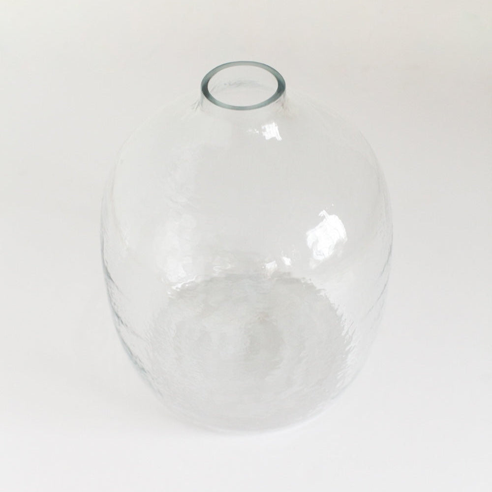 A clear, hand-hammered glass vase with a round shape and a visible textured surface.