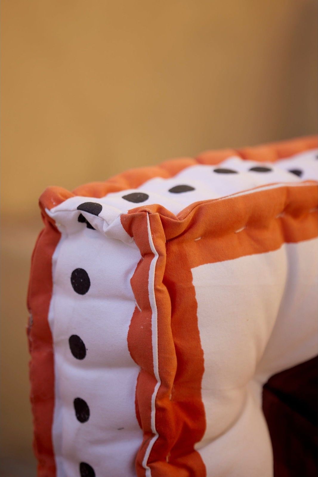 Close-up of a square floor cushion with orange, white, and black details on a blurred background.