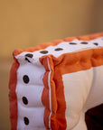 Close-up of a square floor cushion with orange, white, and black details on a blurred background.