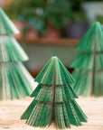 Three green paper Christmas trees on a wooden surface with a blurred background