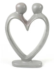 A hand-carved soapstone sculpture depicting two figures holding hands, forming a heart shape, with a predominantly gray color