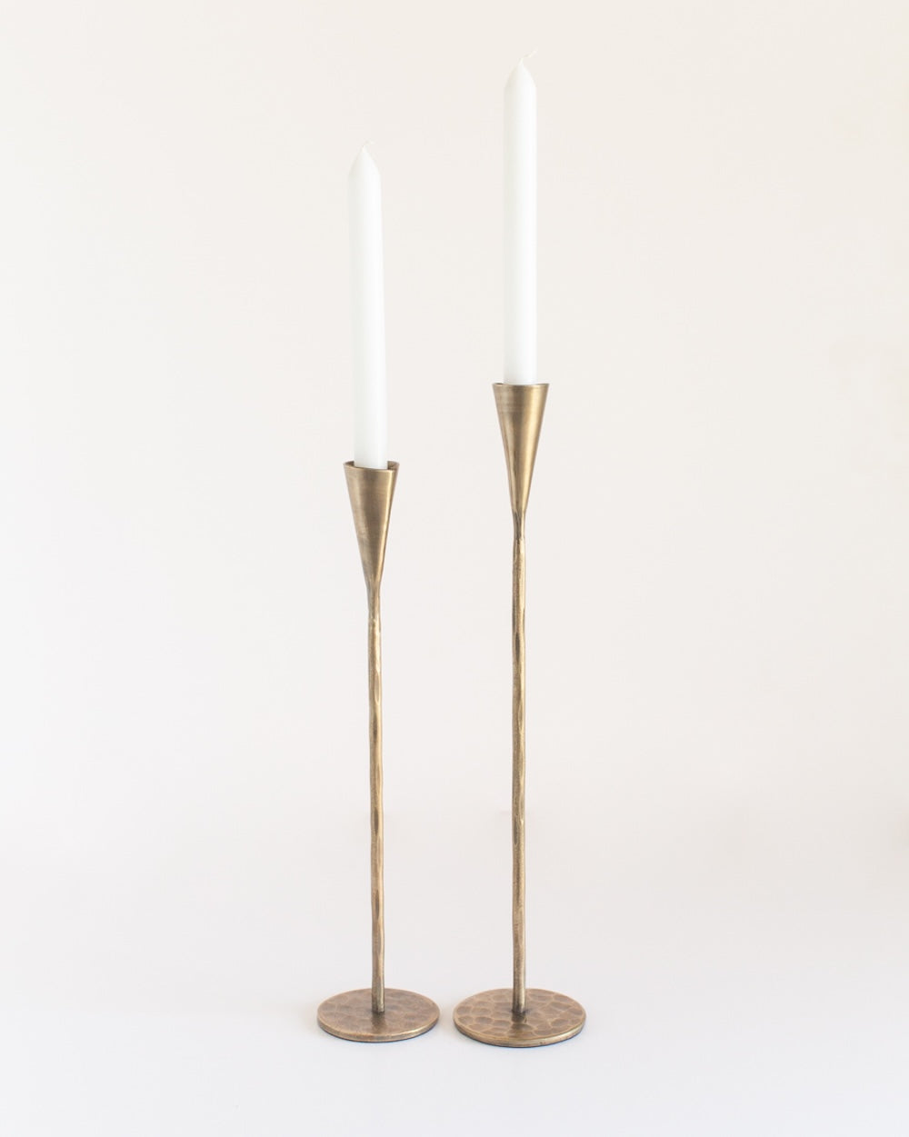 A pair of tall, brass finish iron candle holders with a sleek design, standing upright against a white background.