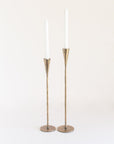 A pair of tall, brass finish iron candle holders with a sleek design, standing upright against a white background.