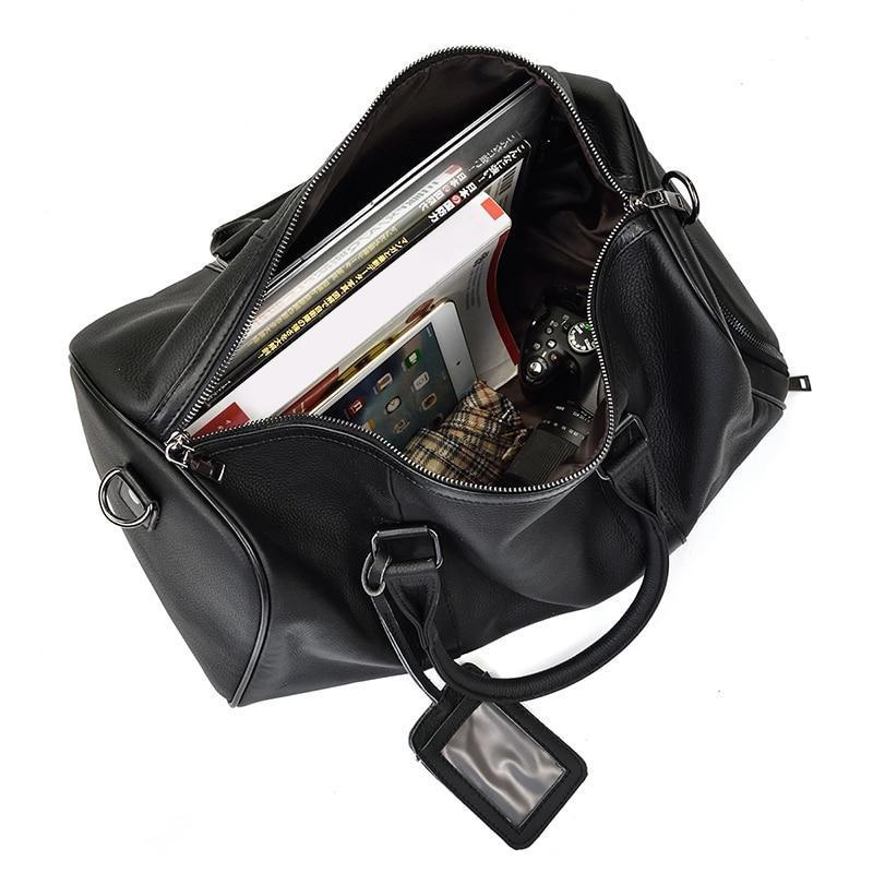 A black leather weekender bag with a leather handle and visible stitching details opened up with books and an umbrella on the inside.