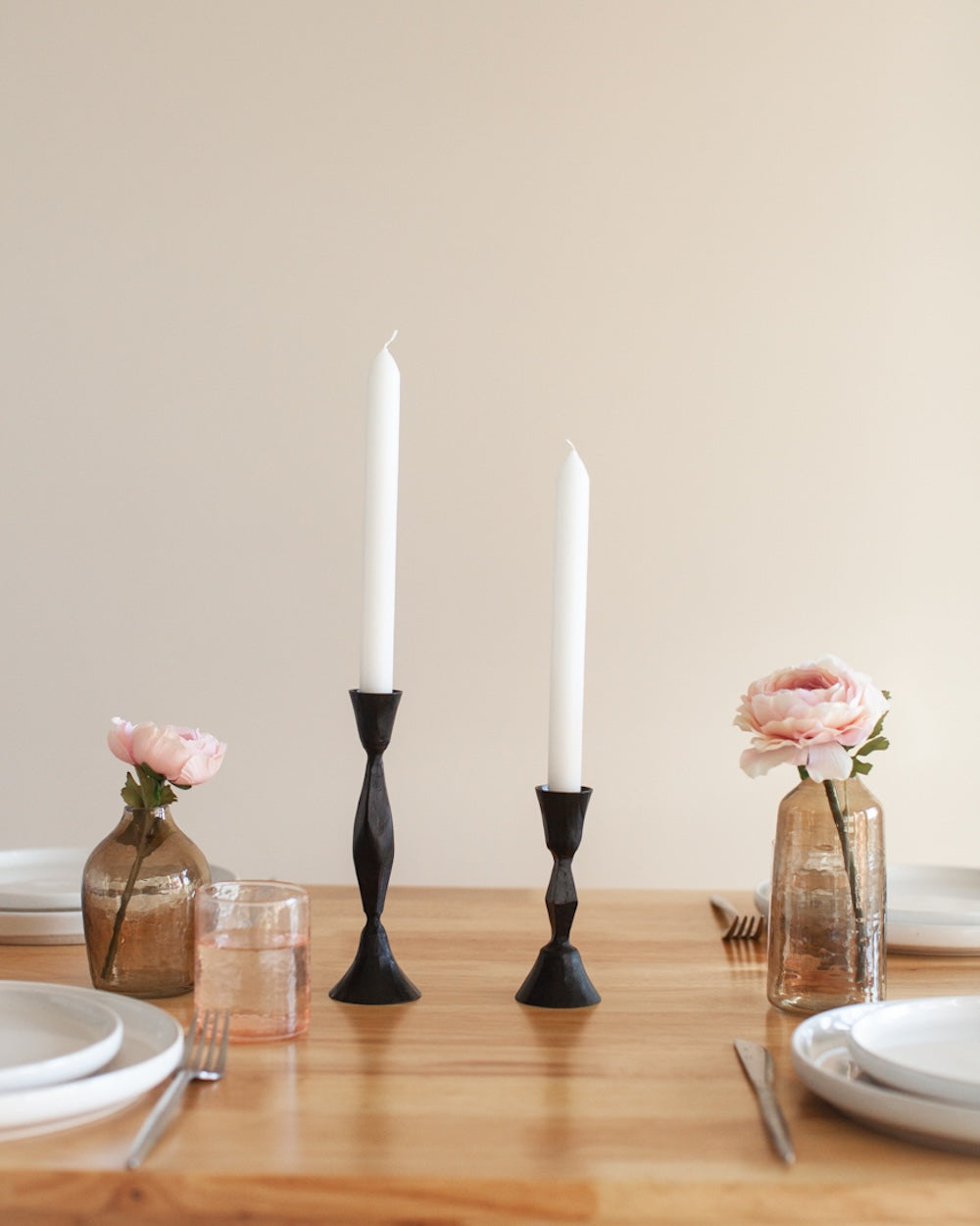Table setting with black candlesticks, pink flowers, and glassware on a wooden table.