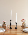 Table setting with black candlesticks, pink flowers, and glassware on a wooden table.