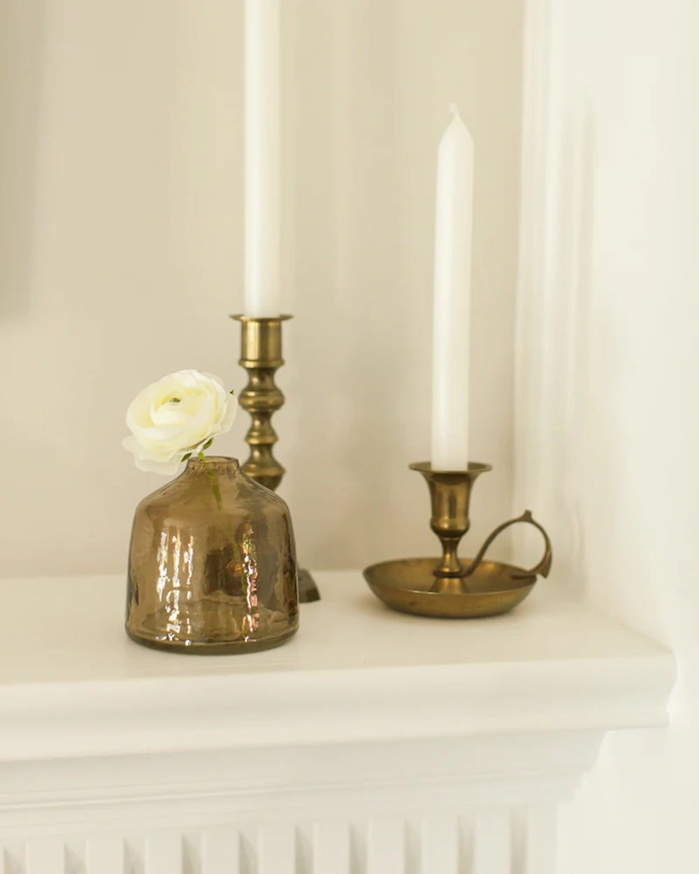 Decorative setup with a vase, candles, and a white flower on a white surface.