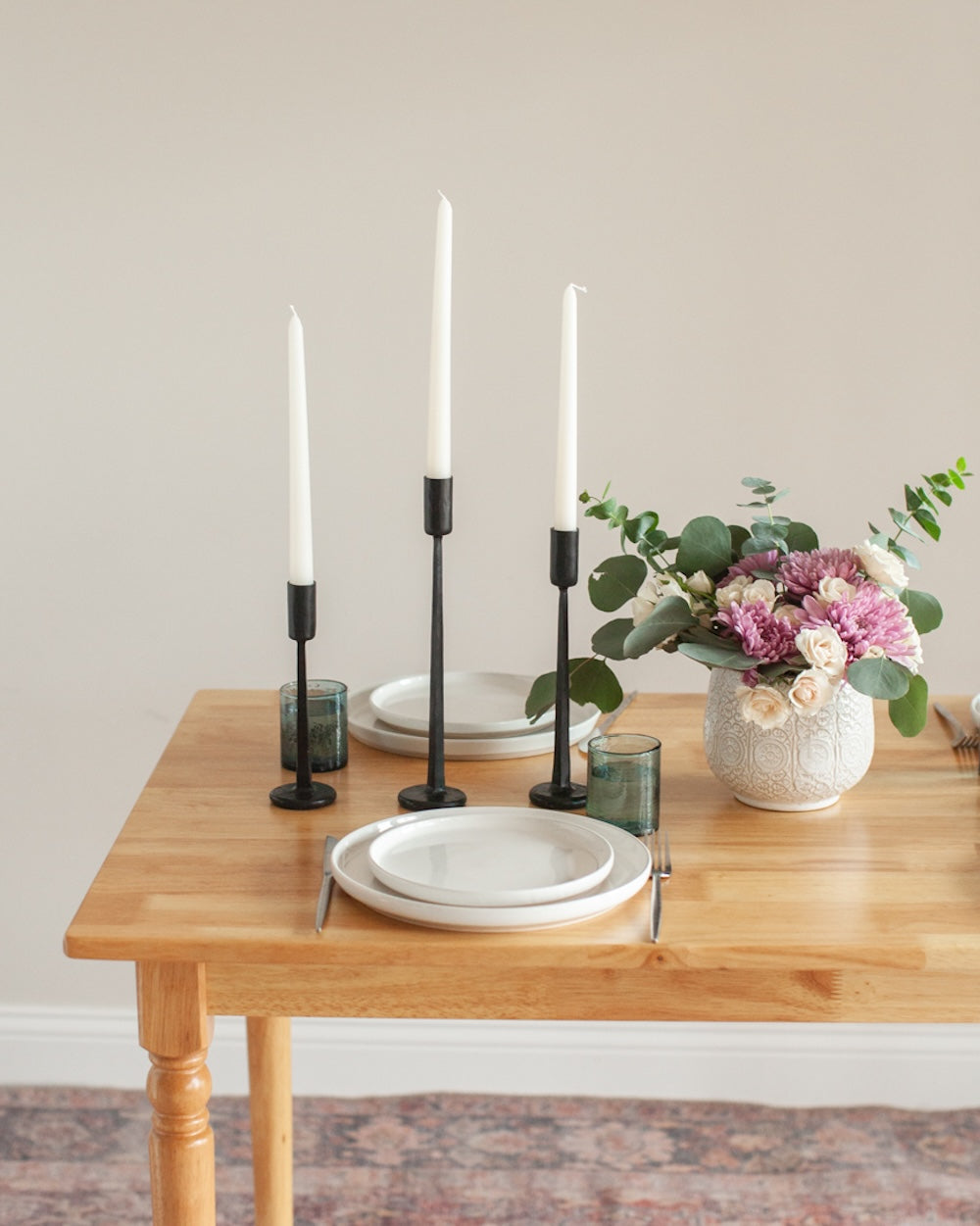 Dining table with white plates, black candle holders, and a vase of flowers.