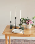 Dining table with white plates, black candle holders, and a vase of flowers.
