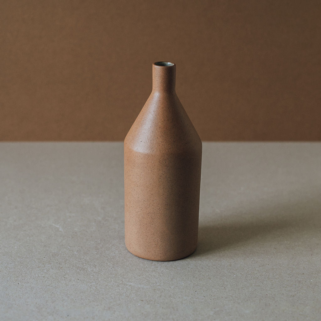 A brown ceramic vase with a narrow neck and a rounded body, placed against a neutral background.