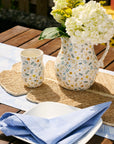Decorative floral pitcher and mug on a wooden table with a blue napkin