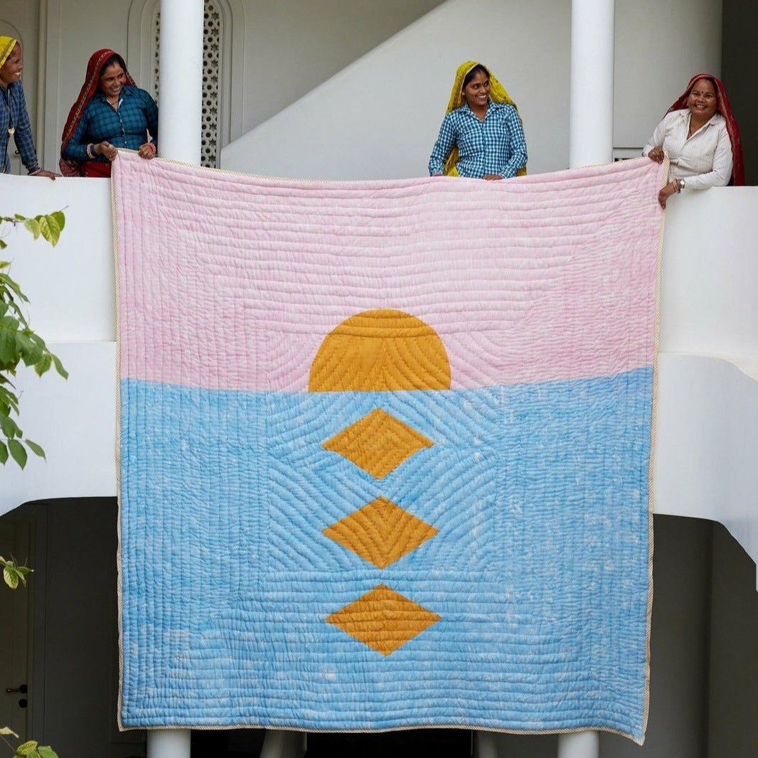 Decorative gold pink and blue quilt being held by artisans