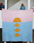 Decorative gold pink and blue quilt being held by artisans