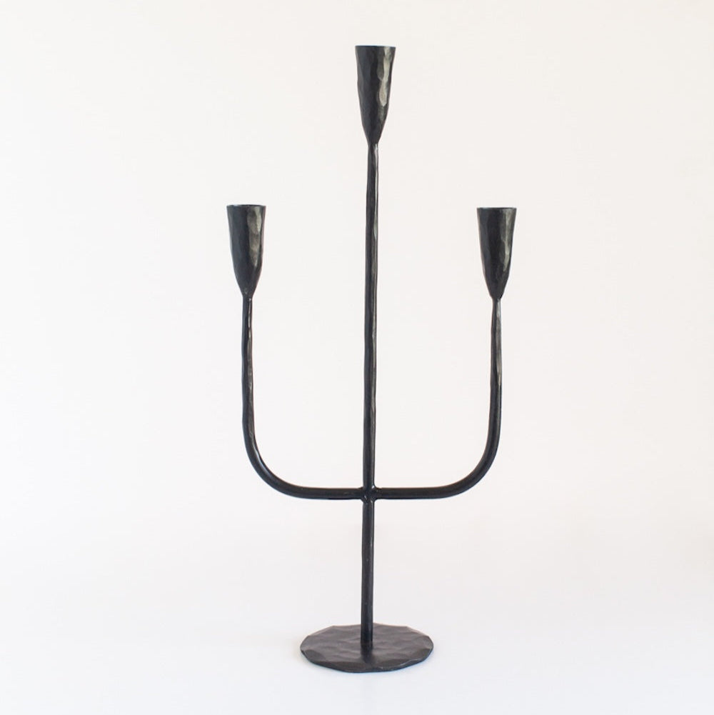 A black iron candelabra with a sturdy weighted base and three arms for holding candles.