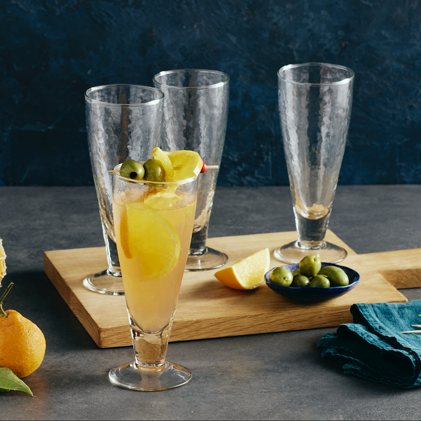 Cocktail glasses with lemon slices and olives on a wooden board against a dark background