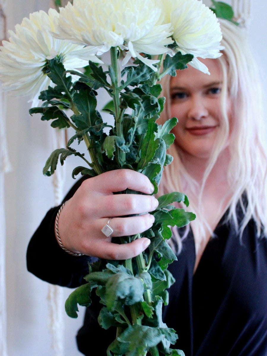 A model wearing a ring made from .925 sterling silver and semi-precious moonstone and holding a bouquet of flowers.