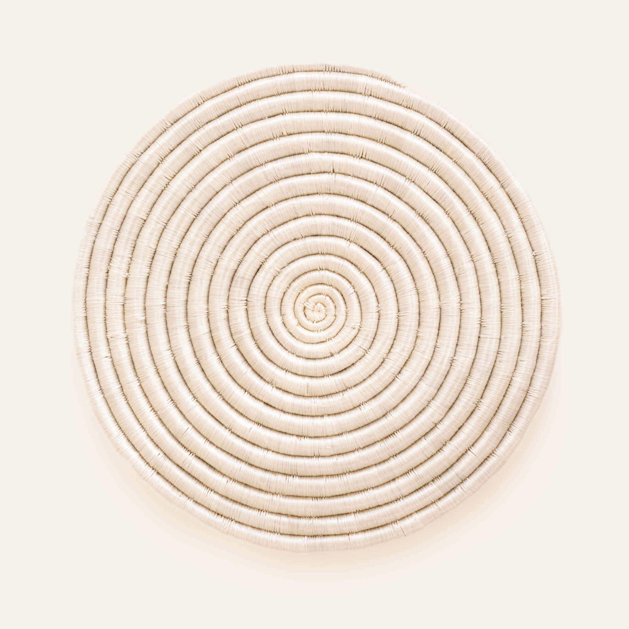 A circular white sisal placemat with a geometric pattern, handwoven with locally sourced sisal