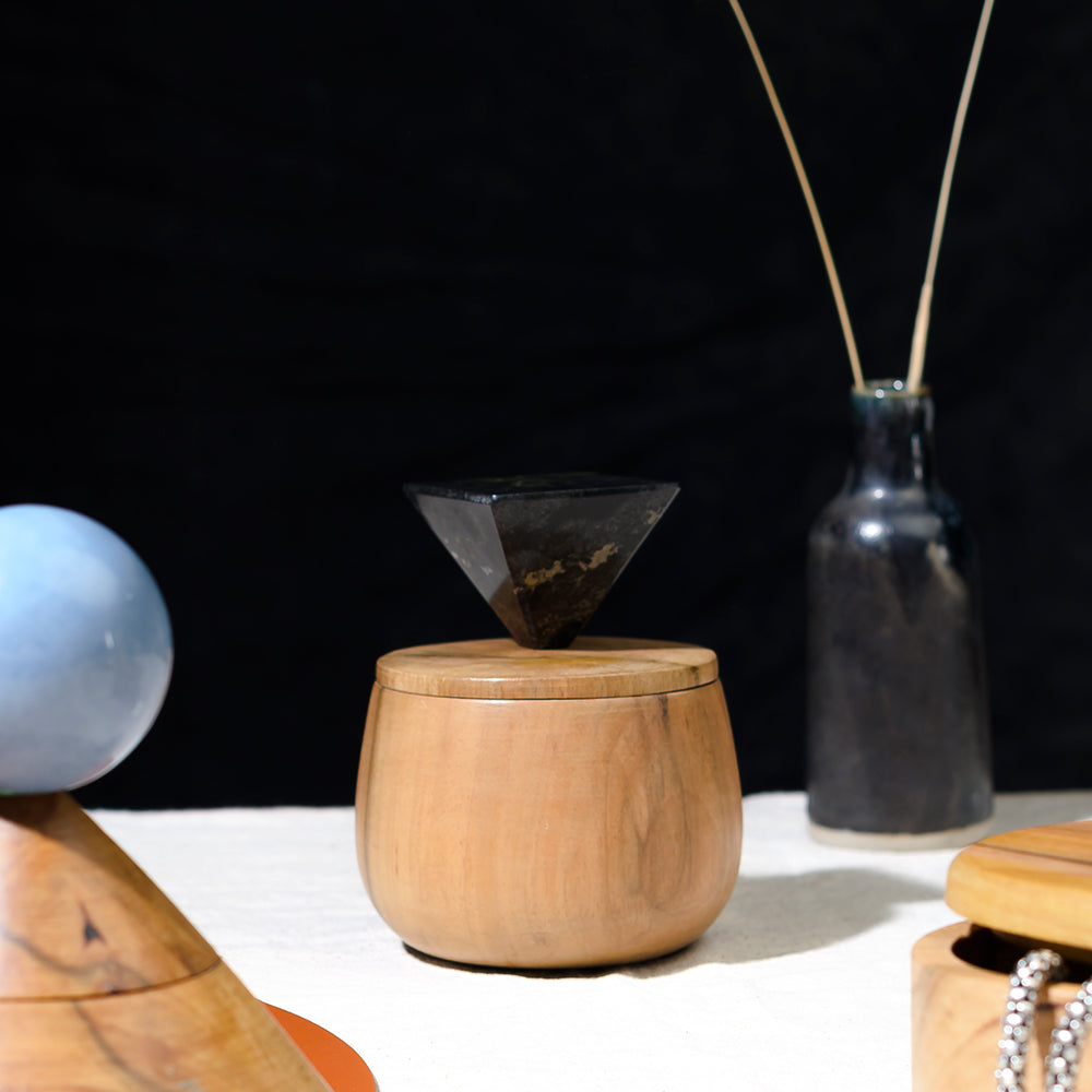 Wooden container with a lid and a small funnel on top, set against a black background.