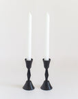 Two black, hand-forged iron candle holders with a textured finish, each holding a white candle.