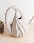 White ceramic swan-shaped vase on a wooden surface with a small potted plant in the background