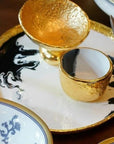 Gold-rimmed ceramic cups on a decorative plate with artistic design