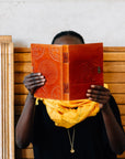 Person holding a red journal in front of their face while sitting on a wooden chair