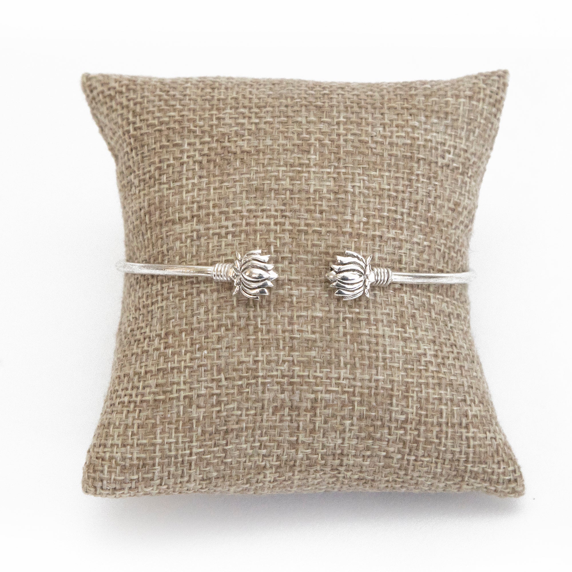 A lotus cuff bracelet with a matte finish displayed on a burlap cushion.
