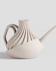 Beige ceramic watering can with wavy design on a light gray background