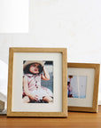 Two wooden picture frames on a wooden surface with photos inside.