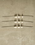 Three metallic cocktail picks on a textured beige surface