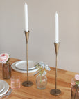 Two gold candle holders with candles on a table setting.
