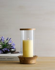 Candle in a glass holder with wooden base on a table with books and flowers.