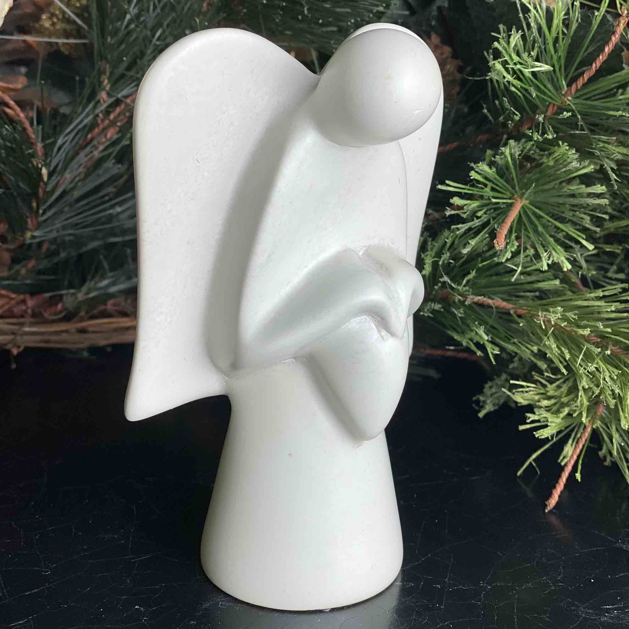 A hand-made stone sculpture of an angel holding a heart in front of a christmas tree