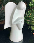 A hand-made stone sculpture of an angel holding a heart in front of a christmas tree