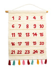 A beige felt advent calendar with red felt numbers from 1 to 25 and colorful cotton tassels hanging on a wooden dowel