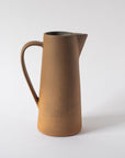 A tall ceramic pitcher with a handle, glazed inside with earth tones and textures