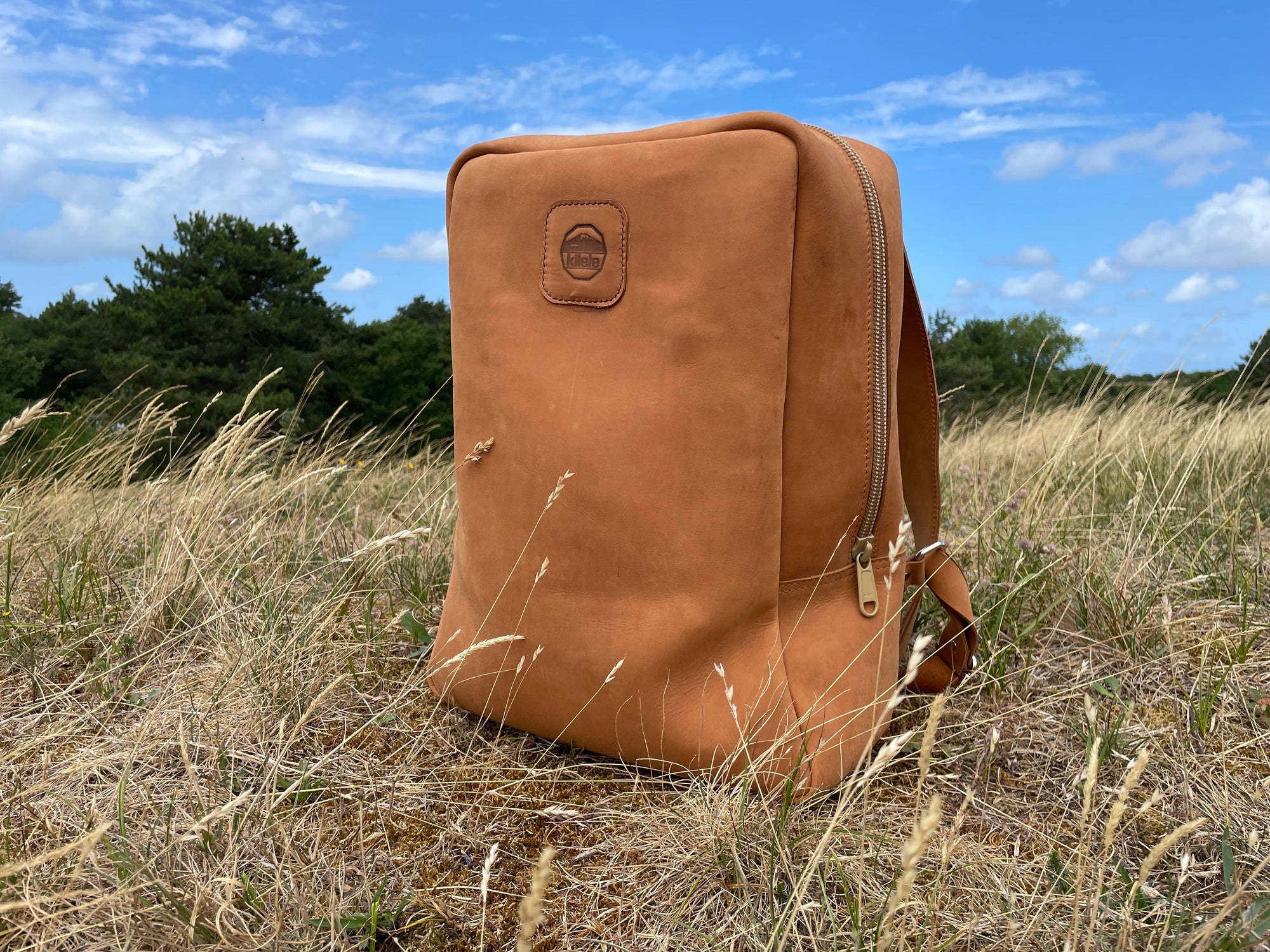 A leather book bag in tan, displayed outside on a field.