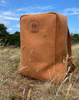 A leather book bag in tan, displayed outside on a field.