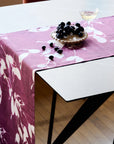 Table with a pink floral tablecloth and blackberries on a white surface.
