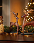 Decorative reindeer and snowman figures on a wooden surface with a blurred Christmas tree in the background.