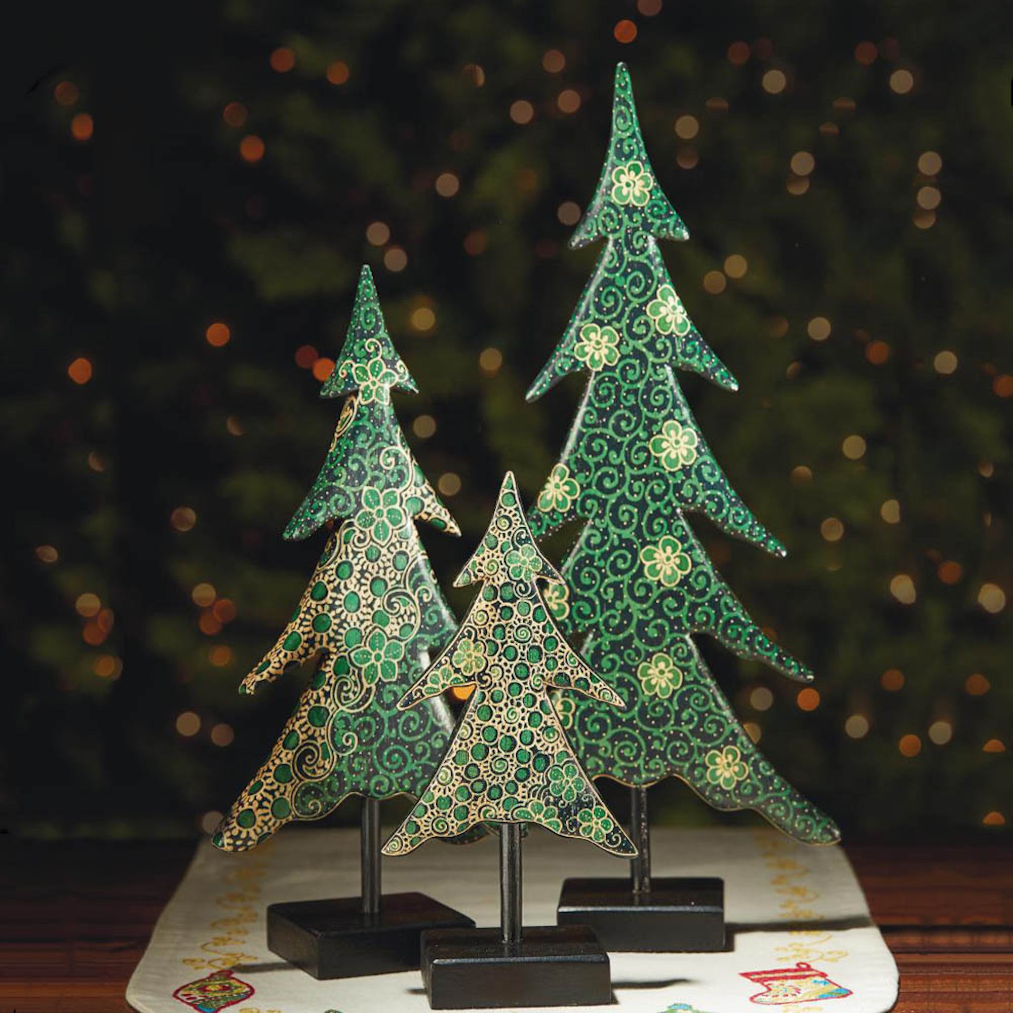 Decorative Christmas trees with intricate patterns on stands against a blurred festive background.