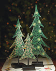 Decorative Christmas trees with intricate patterns on stands against a blurred festive background.