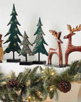 Decorative Christmas trees, reindeer, and snowman on a mantel with garland and lights.