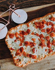A bicycle pizza cutter next to a slice of pizza on a wooden board