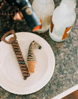 Bottle opener with chain and zebra-patterned bottle cap on a white plate with bottles in the background.