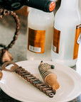 Bottle opener with chain design on a plate, with bottles in the background