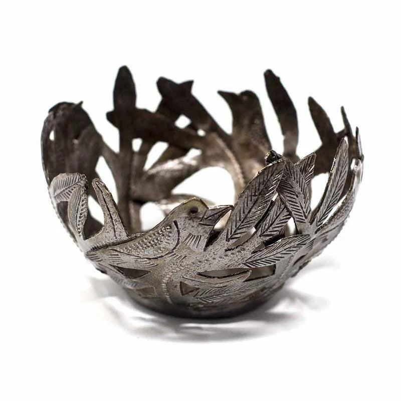 A metal bowl with cut-out bird shapes and leaf patterns, crafted from recycled steel drum, with a darkened patina finish.