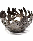 A metal bowl with cut-out bird shapes and leaf patterns, crafted from recycled steel drum, with a darkened patina finish.
