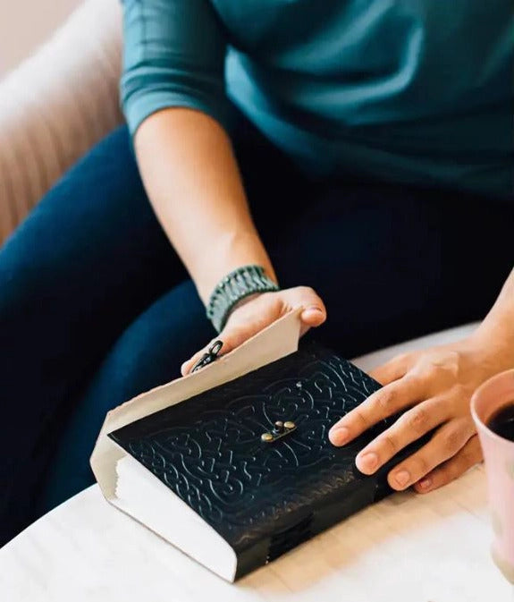 Person holding a black embossed book with a cup of coffee on a light surface