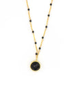 A black beaded gold necklace with a gold-plated chain and a larger black bead as the central piece, displayed against a white background.